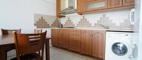 Cocina compacta con armarios de madera, estufa empotrada y lavadora de carga frontal.