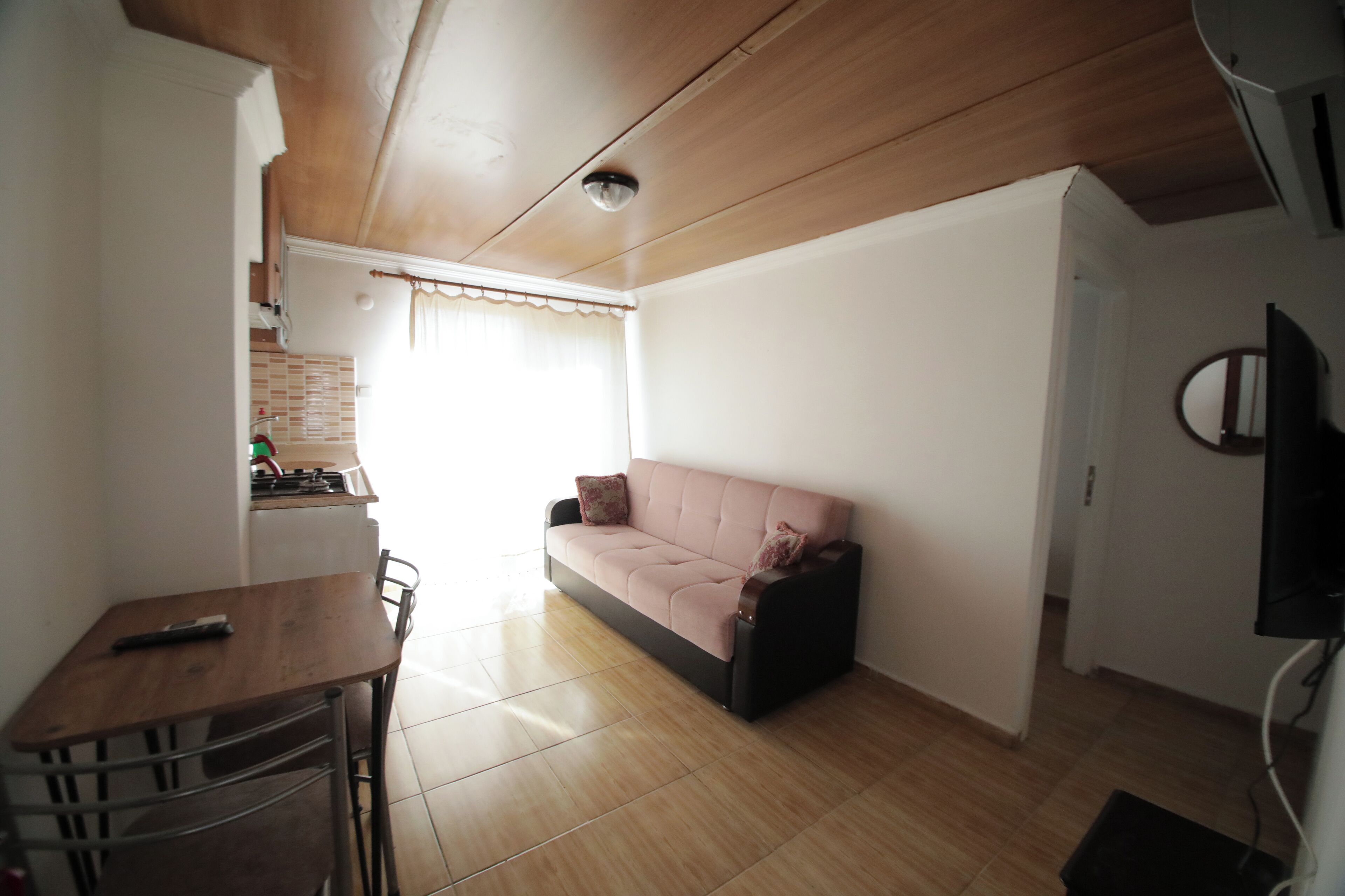 Una sala de estar con un sofá, una mesa de comedor y un televisor instalado en la pared.