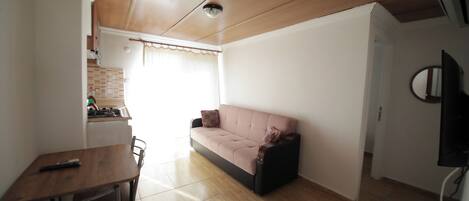 Una sala de estar con un sofá, una mesa de comedor y un televisor instalado en la pared.