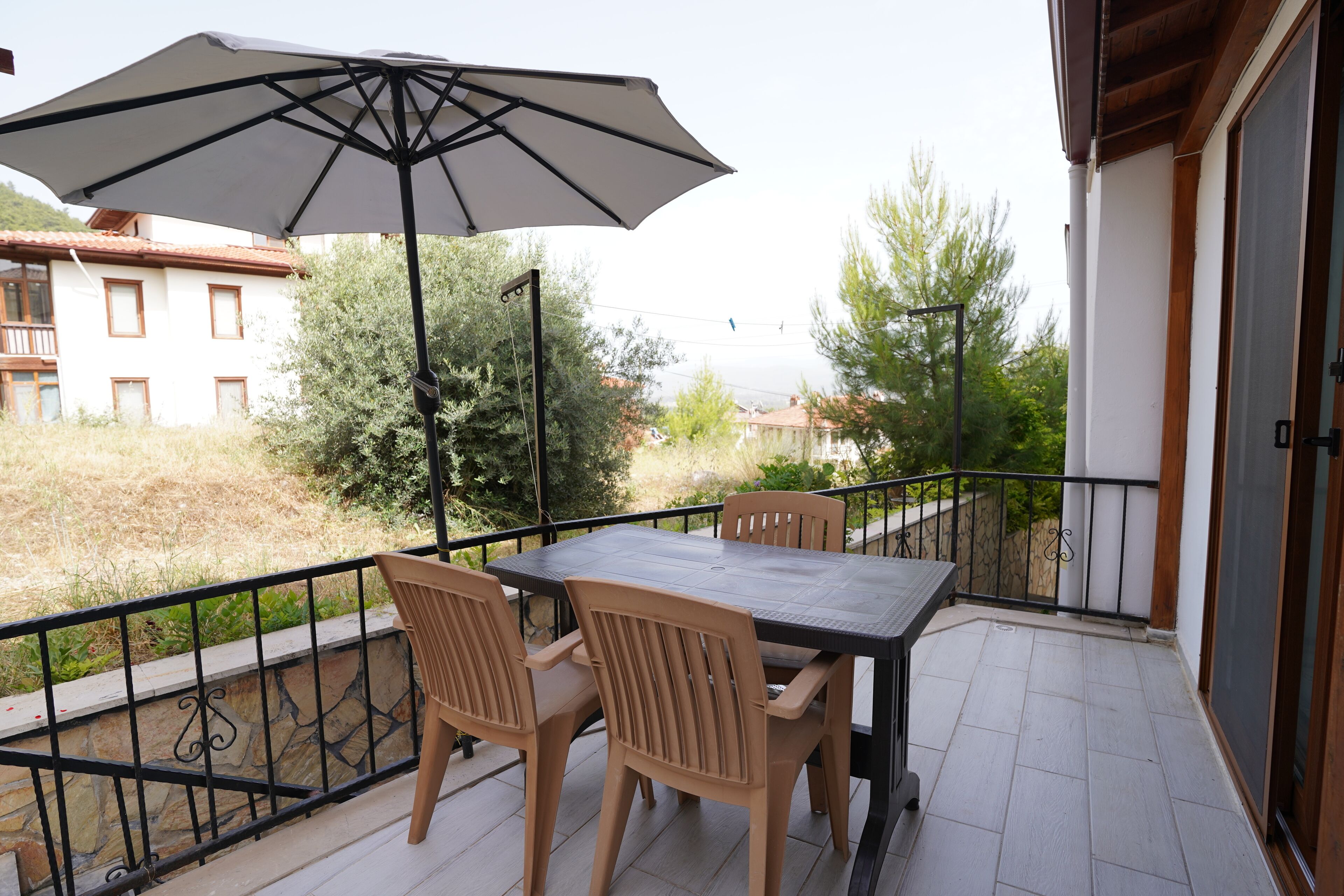 A balcony with a table and chairs, a large umbrella, and a view of buildings and trees.