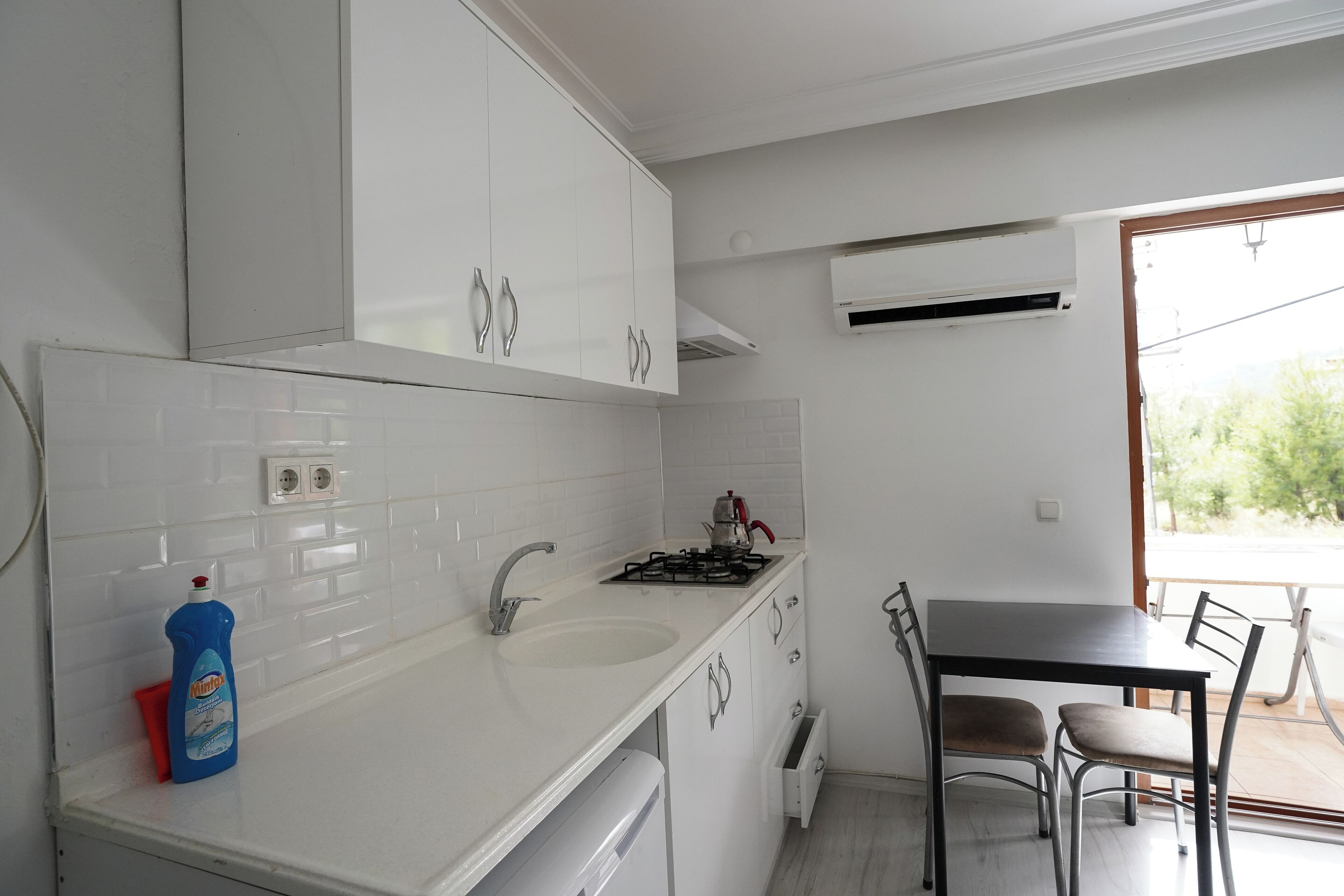A modern kitchen with white cabinets, a sink, a stove, and a dining area with chairs.