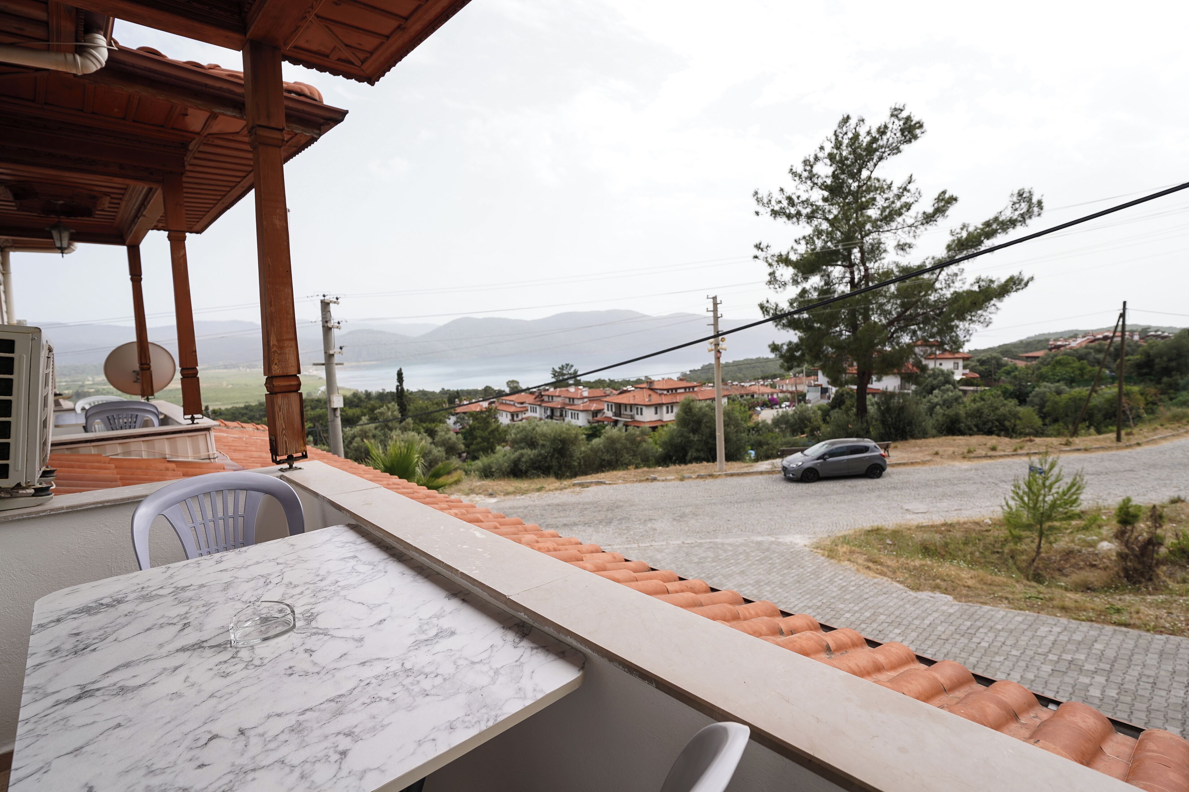 A terrace with a marble table and chairs, overlooking a residential area with houses and a car on the street.