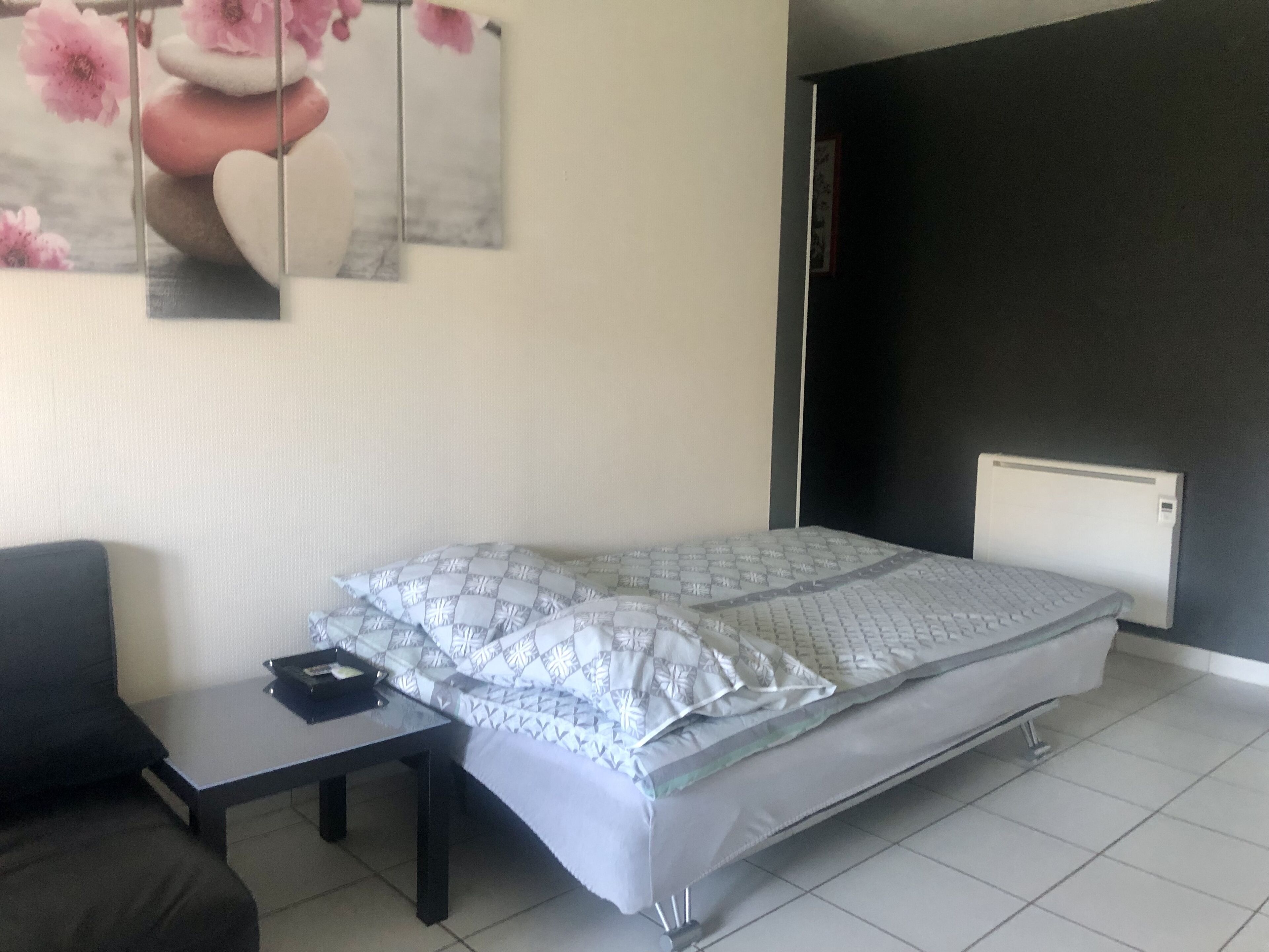 Een slaapkamer met een bed, een klein tafeltje, een stoel en een wanddecoratie.