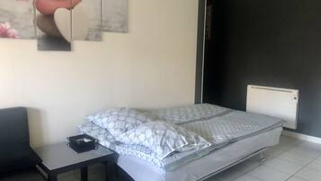 Een slaapkamer met een bed, een klein tafeltje, een stoel en een wanddecoratie.