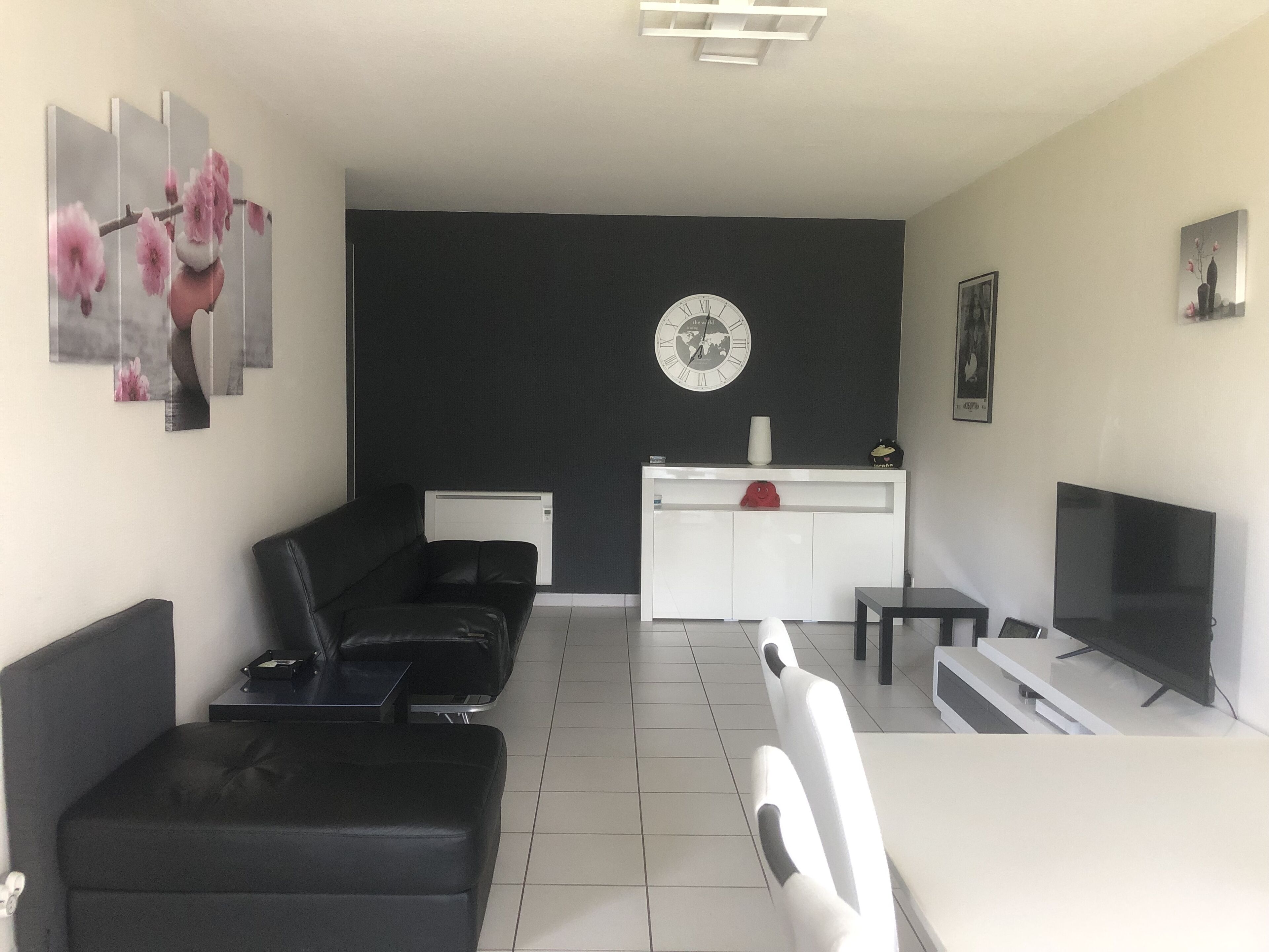 Un saló modern amb un sofà negre, una taula de menjador, un televisor i un moble blanc.