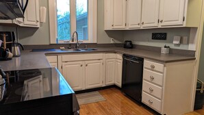 A kitchen with white cabinets, a dishwasher, a sink, and a window. - Waldheim Cottage: In-town bar Harbor Hideaway (Bar Harbor)