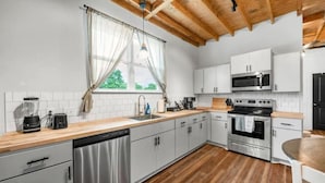 A modern kitchen with white cabinets, stainless steel appliances, and a wooden ceiling. - Homely Haven Near A&M (Bryan)