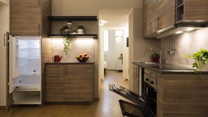 A modern kitchen with wooden cabinets, a built-in oven, and a countertop with a bowl of fruit and a potted plant. - notaMi - Voghera Fashion District (Milan)
