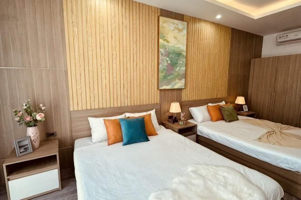 A hotel room with two beds, wooden paneling on the walls, a painting, and a nightstand with a lamp.