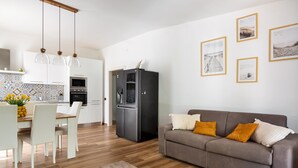 Une cuisine moderne avec des meubles blancs, un coin repas avec une table et des chaises, un canapé gris avec des coussins orange et des tableaux encadrés au mur.