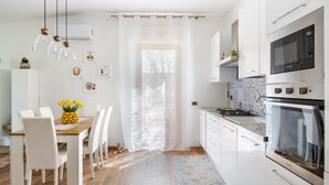 Une cuisine moderne avec des meubles blancs, un four encastré et un coin repas comprenant une table en bois et des chaises blanches.