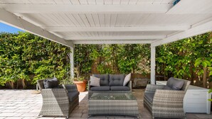 Une terrasse extérieure dotée de meubles en osier, d’un plafond blanc et d’une végétation luxuriante.