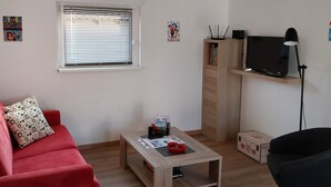 A modern living room with a red sofa, a wooden coffee table, a TV on a shelf, and a lamp.
