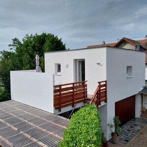 A modern white building with a flat roof, a small balcony with wooden railings, and a door leading to an interior space. - L'egelbach (Uffholtz)