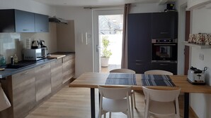 A modern kitchen with wooden cabinets, a dining table with chairs, a microwave, a kettle, and an oven.