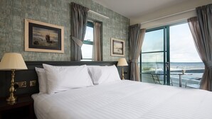 A hotel room with a large bed, two bedside lamps, a framed picture on the wall, and a view of the sea through the window. - The Tynemouth Castle Inn - The Inn Collection Group (North Shields)