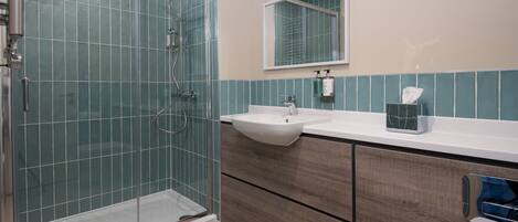 Un baño con cabina de ducha de vidrio, un lavamanos y un mueble de tocador con cajones.