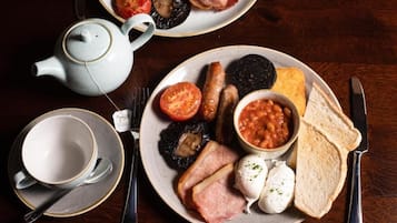 Une table dressée pour le petit-déjeuner avec des assiettes contenant des œufs, des saucisses, des tomates, des haricots et des toasts.