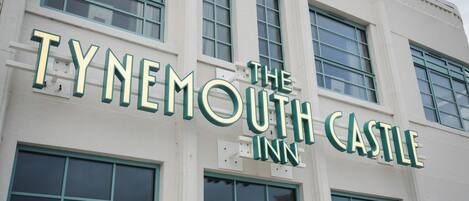 The exterior of The Tynemouth Castle Inn with large windows and a prominent sign.