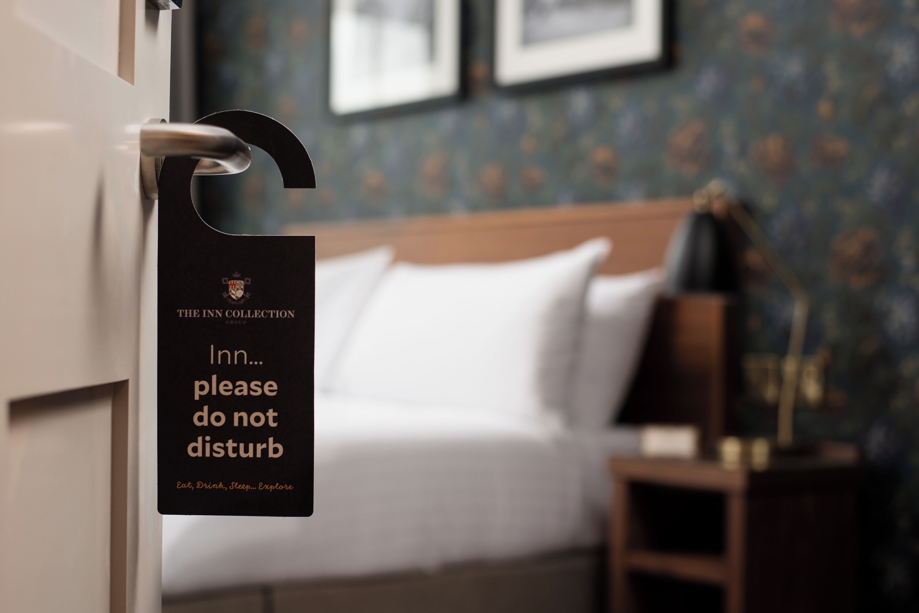 A hotel room with a bed, a nightstand, and a sign on the door that reads "The Inn Collection please do not disturb."