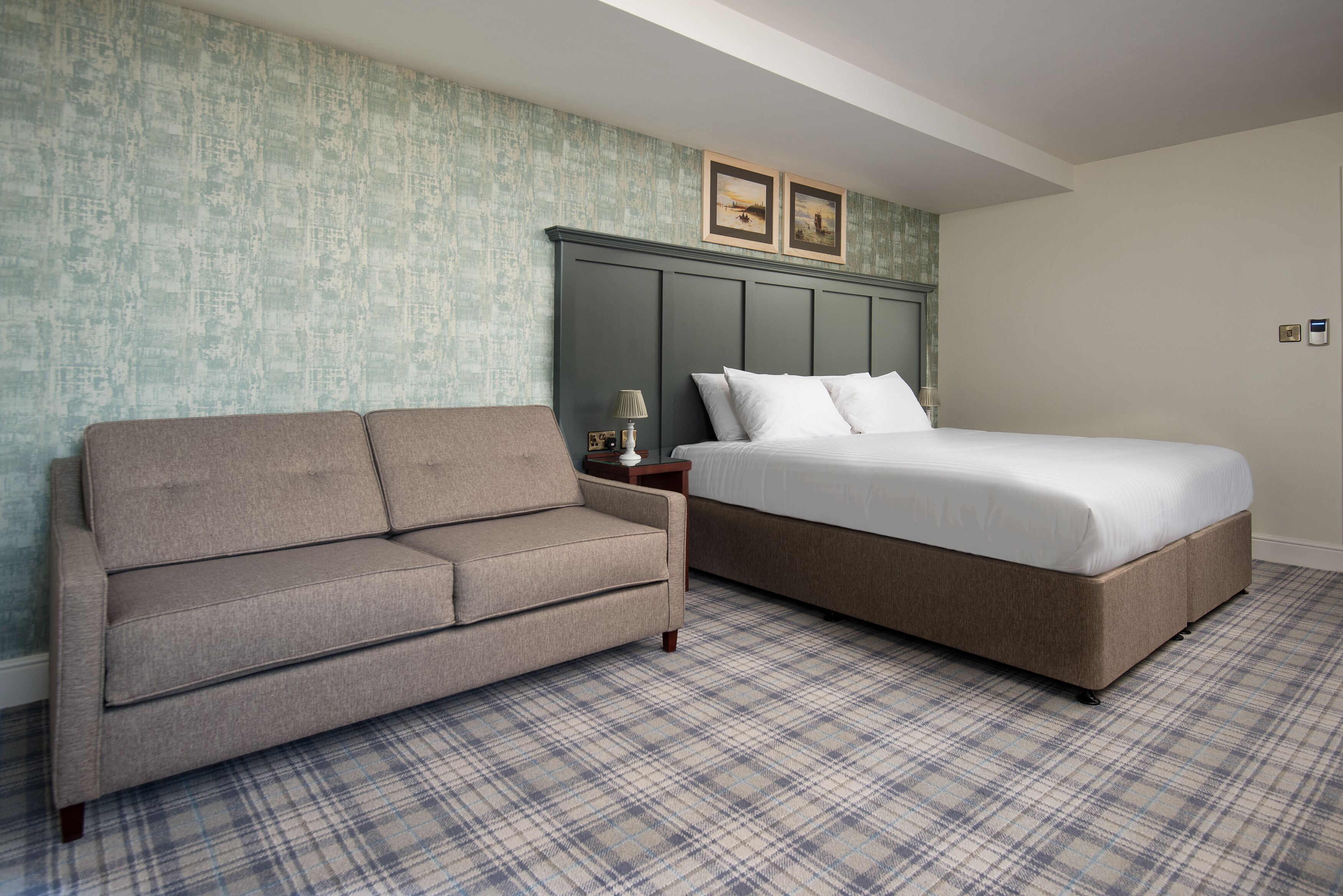A hotel room with a bed, a sofa, a plaid carpet, and a textured wall.