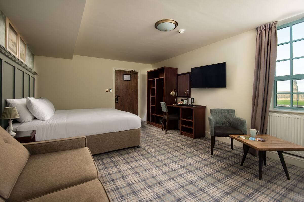 A hotel room with a bed, a desk, a chair, a table, and a TV.