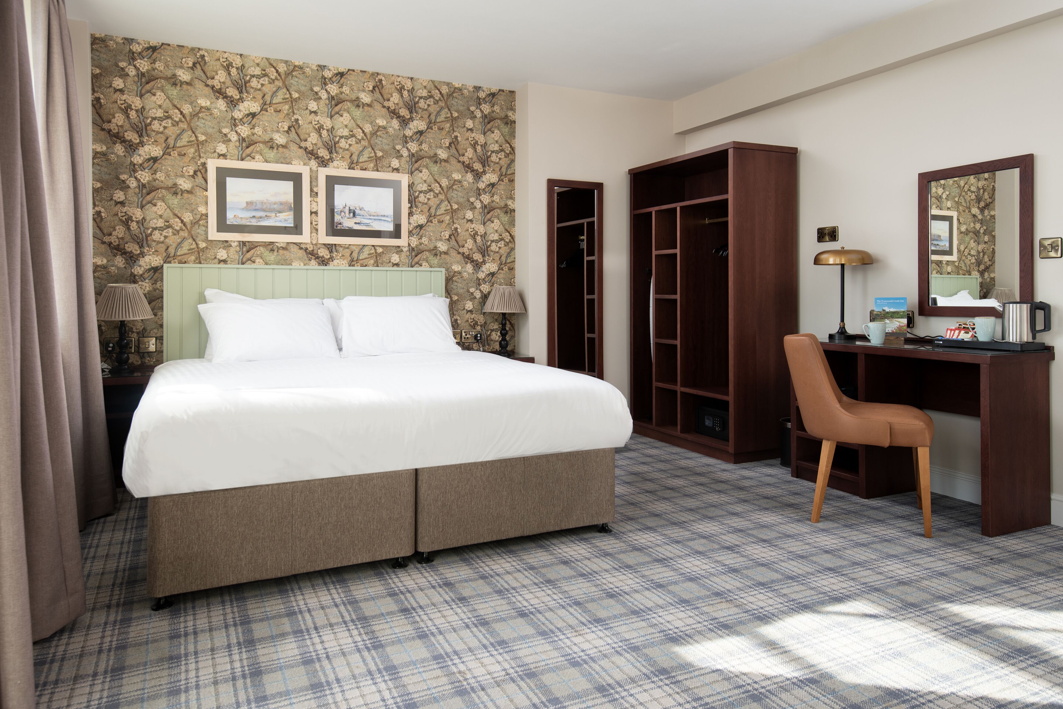 A hotel room with a large bed, a desk, a chair, and a wardrobe.