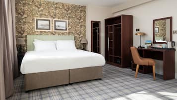 A hotel room with a large bed, a desk, a chair, and a wardrobe.