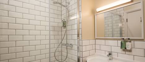 A bathroom with white tiled walls, a glass shower enclosure, a sink with a mirror, and a soap dispenser.