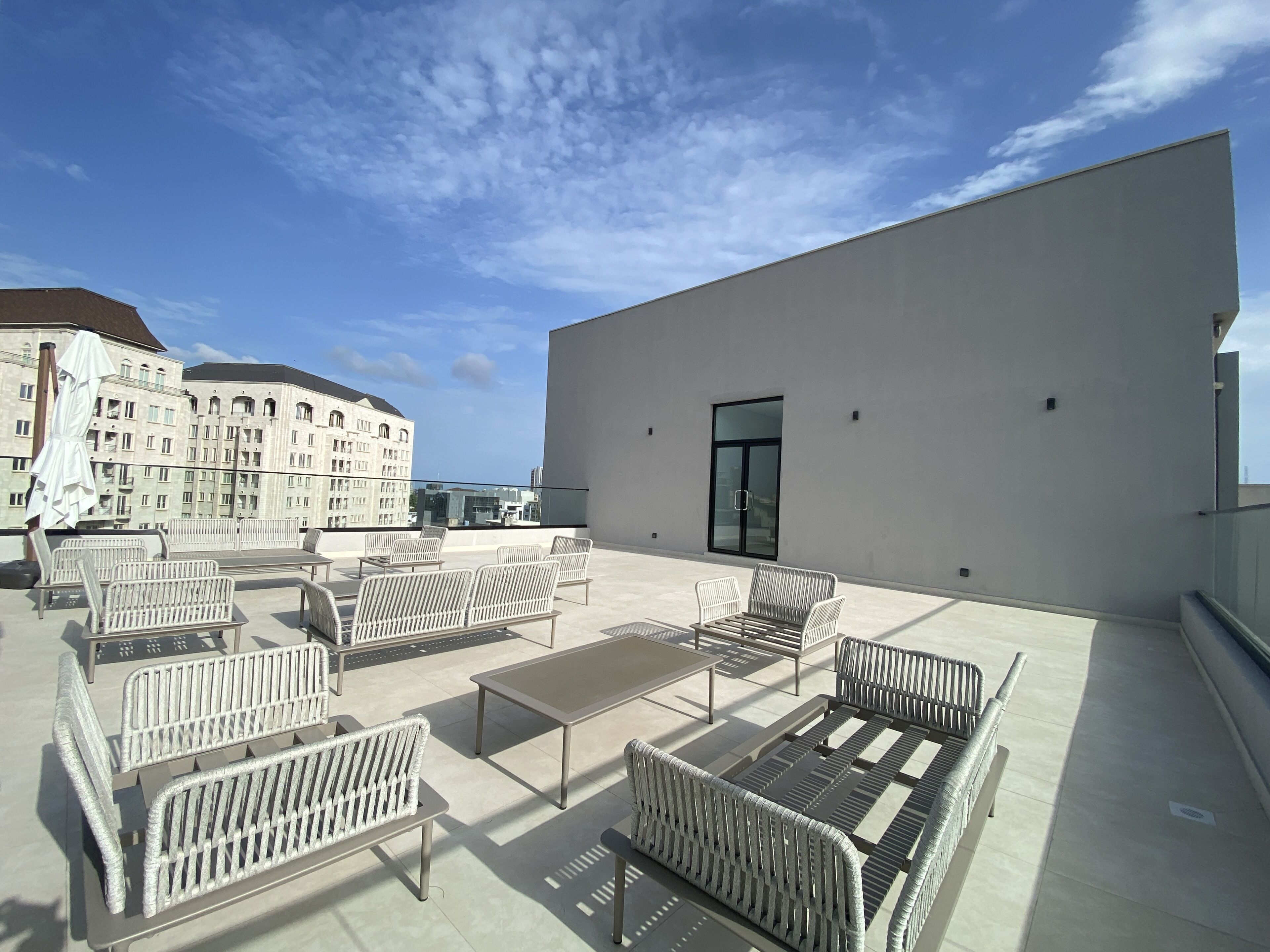 Una terraza en la azotea con mobiliario exterior y vistas a un edificio al fondo.