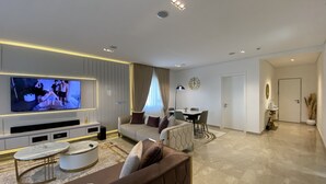 A modern living room with a flat-screen TV, a sofa, a coffee table, and a dining area with a table and chairs. - Mastermindsluxuryliving (Lagos)