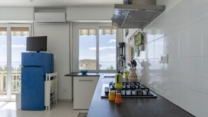 A modern kitchen with a gas stove, a blue refrigerator, and a window with a view of the sea.