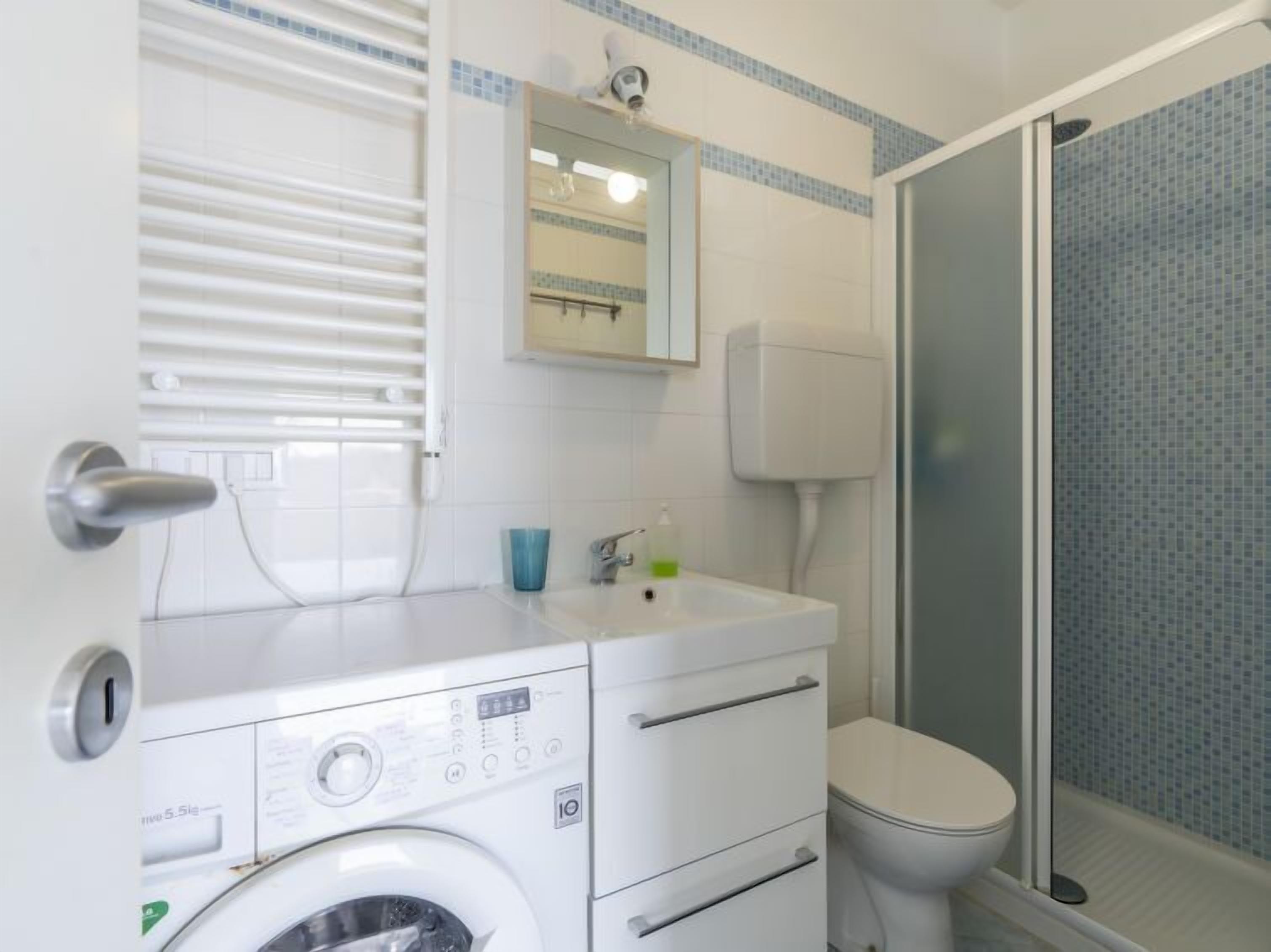Ein kleines Badezimmer mit Waschmaschine, Toilette und Duschbereich.