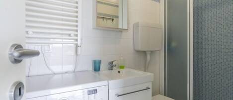 Ein kleines Badezimmer mit Waschmaschine, Toilette und Duschbereich.