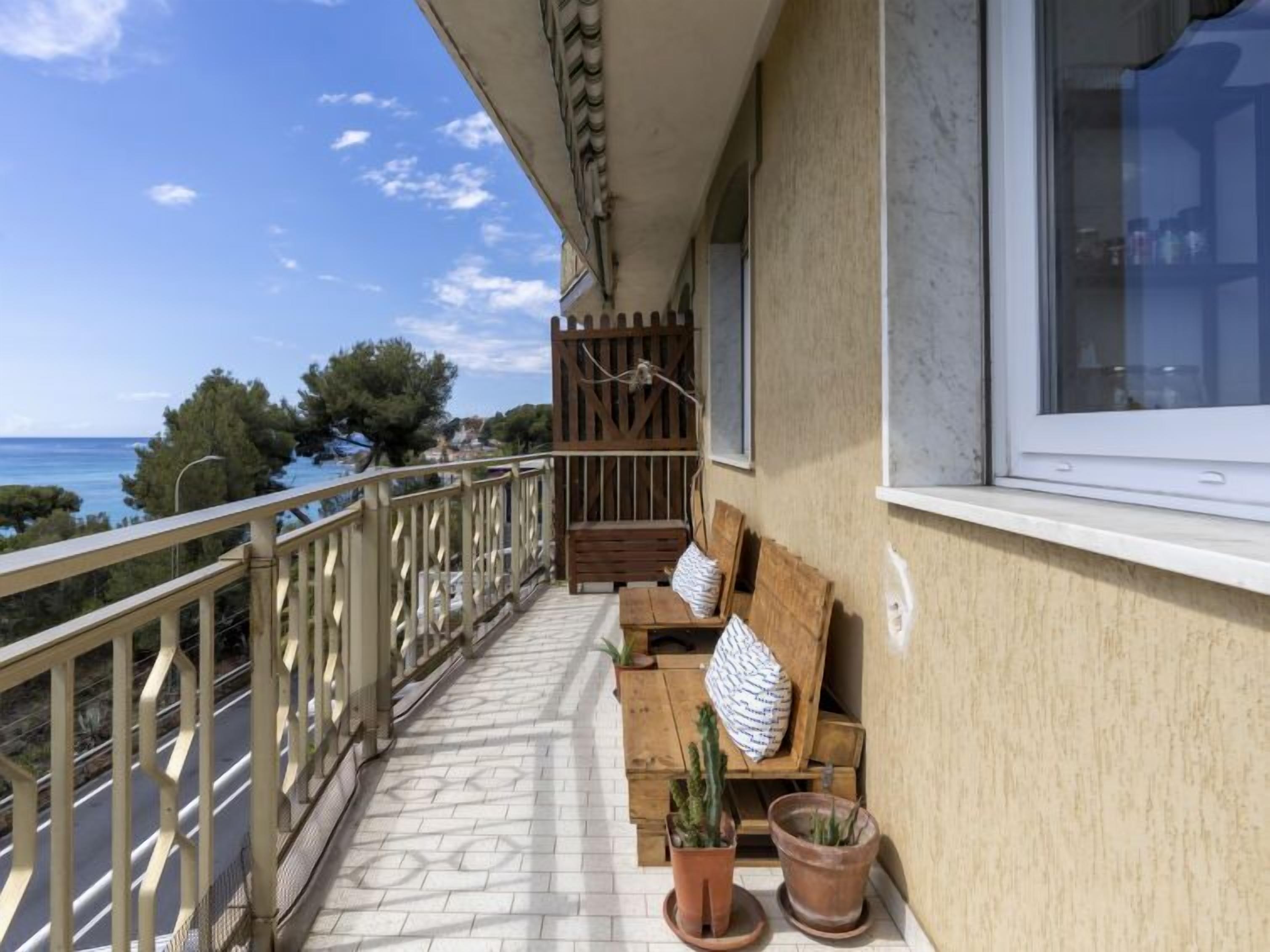 Ein Balkon mit einer Holzbank, zwei Blumentöpfen und Blick auf das Meer.