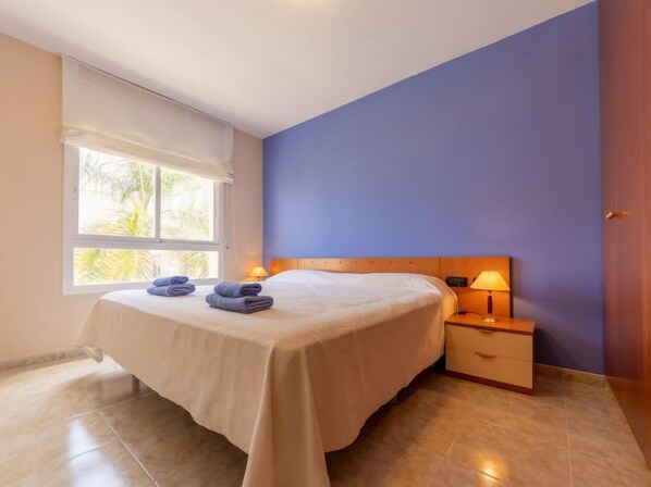 A bedroom with a bed, two bedside tables, a window with curtains, and a view of greenery outside.