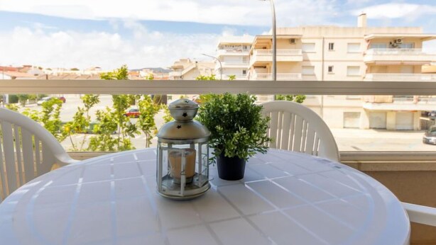 Ein runder Tisch mit weißer Tischdecke, einer Laterne und einem Blumentopf auf einem Balkon mit Blick auf eine Wohngegend.