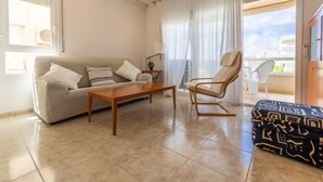 Ein Wohnzimmer mit einer Couch, einem Holztisch, einem gemusterten Hocker, einem Sessel und einem Balkon mit Blick.