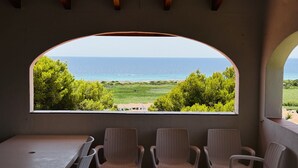 A room with a large arched window overlooking a beach and ocean. There are four wicker chairs and a table in the room. - Seaviews AC viilla 8 people near beach (Son Bou)