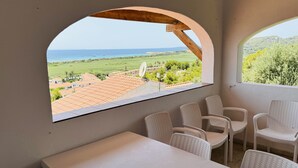 A room with a large arched window overlooking a coastal landscape, a white table, and several wicker chairs. - Seaviews AC viilla 8 people near beach (Son Bou)
