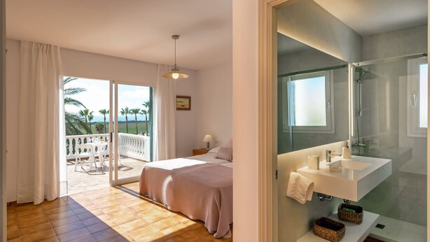 Un dormitorio con balcón, un baño con ducha de vidrio y vistas a palmeras.