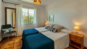 Una habitación con dos camas, una silla, una mesita de noche y una lámpara colgante.