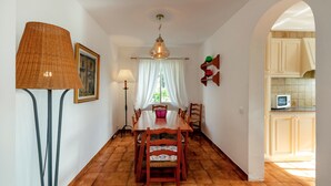 Un comedor con una mesa y sillas de madera, una lámpara colgante y vista a la cocina.
