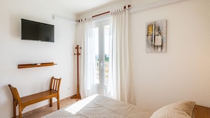 Ein Schlafzimmer mit einem Bett, einem Holzstuhl, einem an der Wand befestigten Fernseher und einem Bild an der Wand.