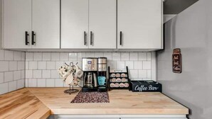 A modern kitchen with white cabinets, a coffee machine, a coffee bar, and a decorative vase. - 5-Star 2BR: Clean, Comfy, SuperHost Hospitality (Bryan)