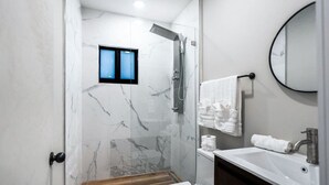Un baño moderno con ducha de vidrio, suelo de madera, lavamanos blanco y pared de mármol.