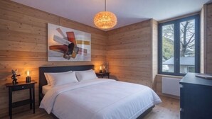 A bedroom with a bed, wooden walls, a ceiling light, a window, and a nightstand with a lamp. - Apartment overlooking Mont Blanc with parking (Chamonix-Mont-Blanc)