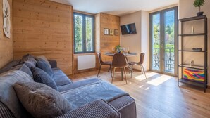 A cozy living room with a sofa, a dining table with chairs, a TV mounted on the wall, and a balcony with a railing. - Apartment overlooking Mont Blanc with parking (Chamonix-Mont-Blanc)