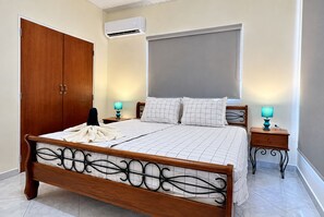 Een slaapkamer met een houten bed, twee nachtkastjes met lampen, een kledingkast, een airconditioning en een groot raam.