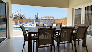 Un patio cubierto con piscina, sillones de descanso y una mesa de comedor con sillas.